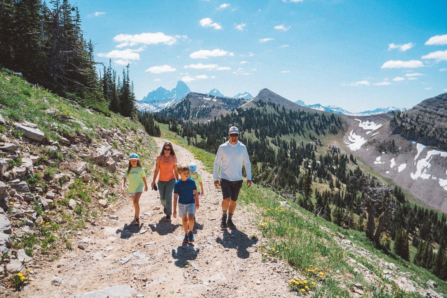 Family hiking on a mountain trail under a clear blue sky.