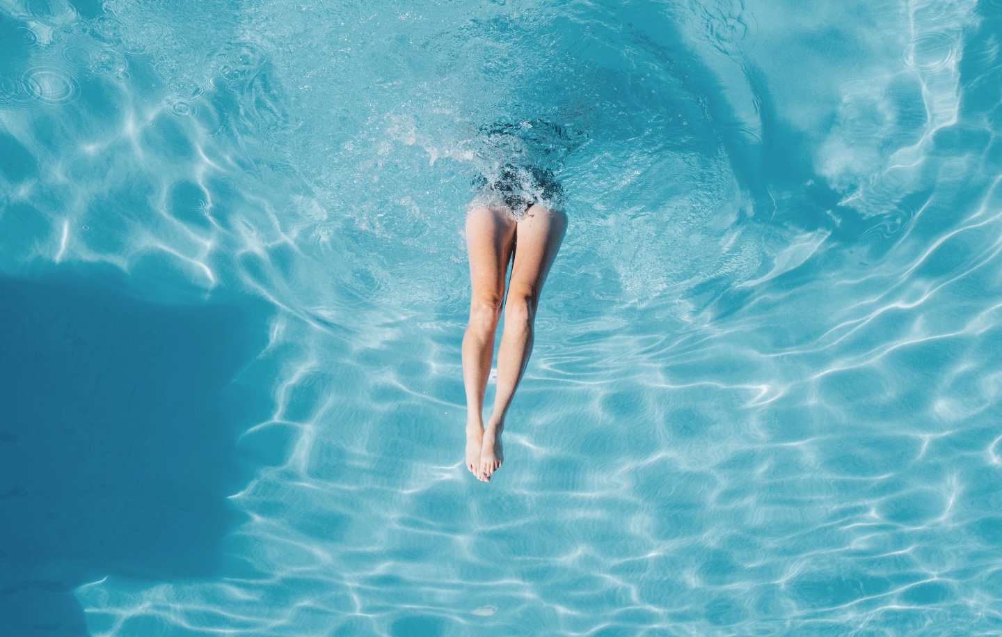 Person diving into a pool, legs visible above water.