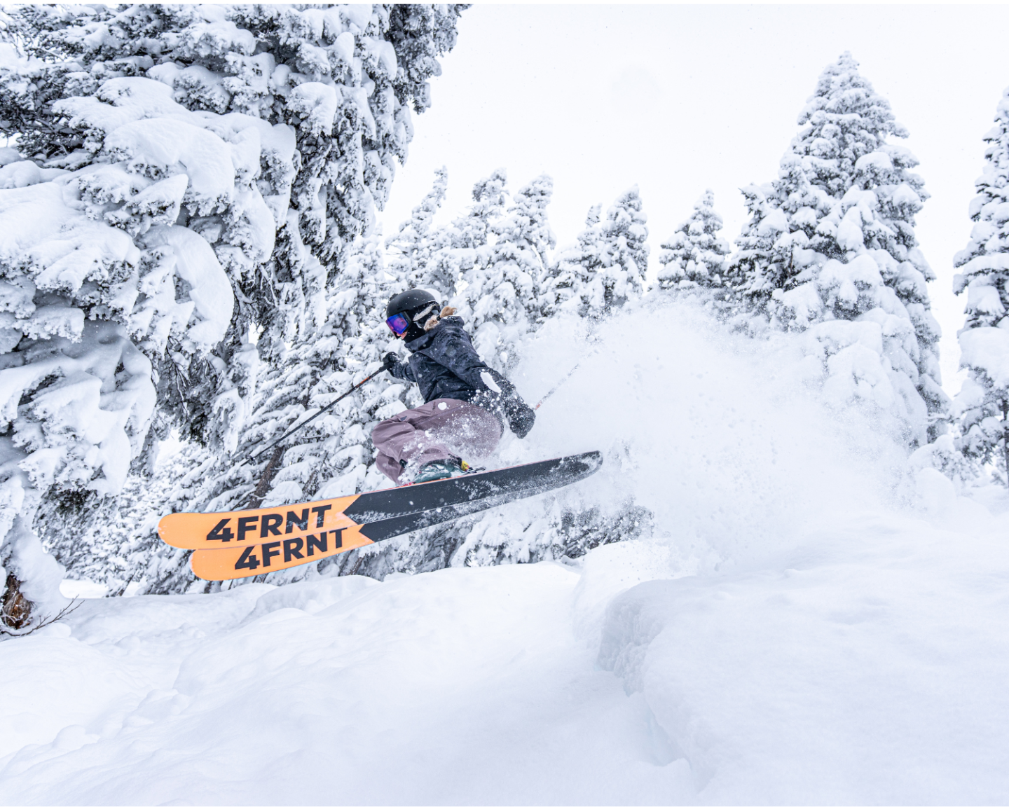 Skier in snowy forest, mid-jump, wearing goggles and helmet.