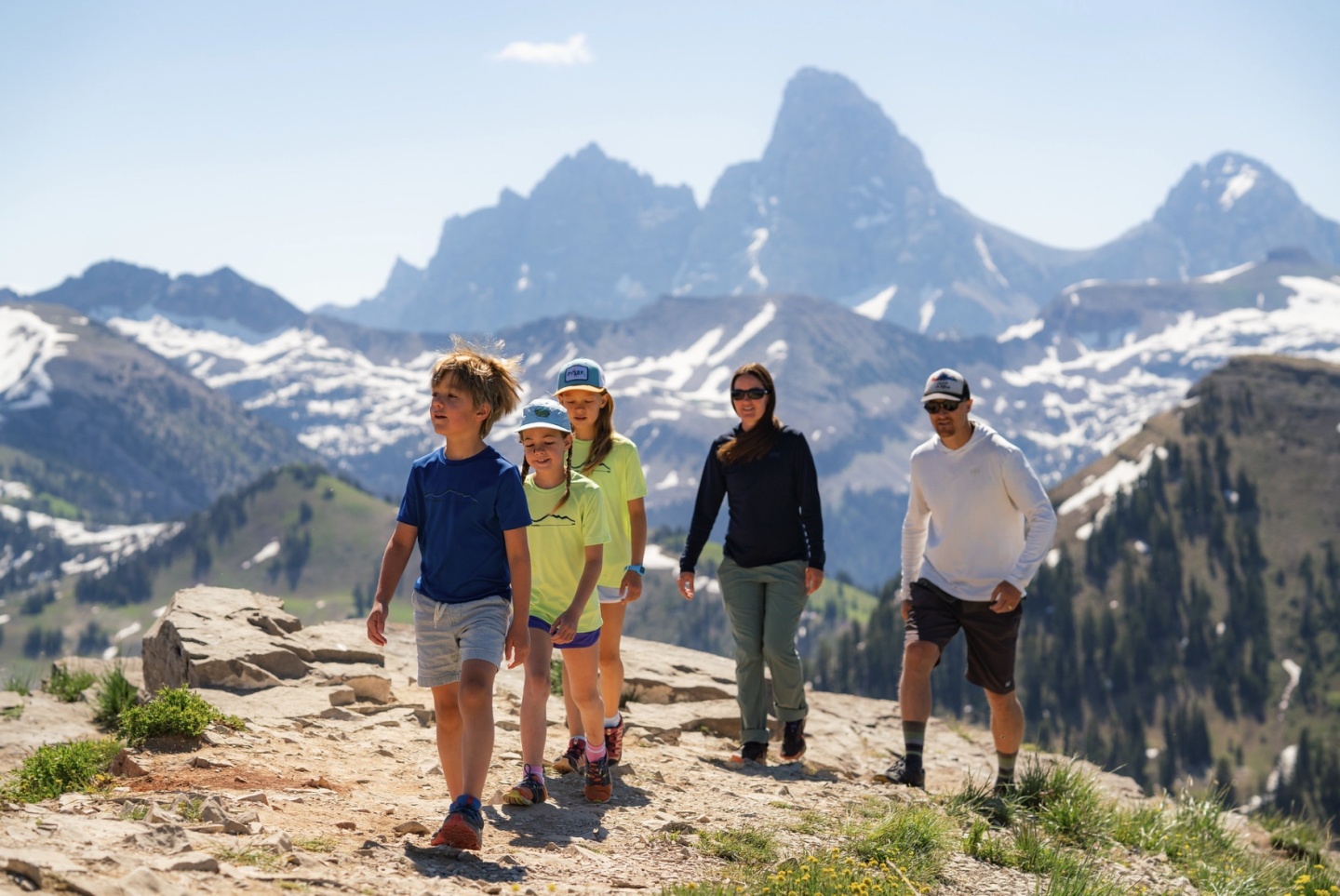 Group hiking on a mountain trail with snow-capped peaks in the background.