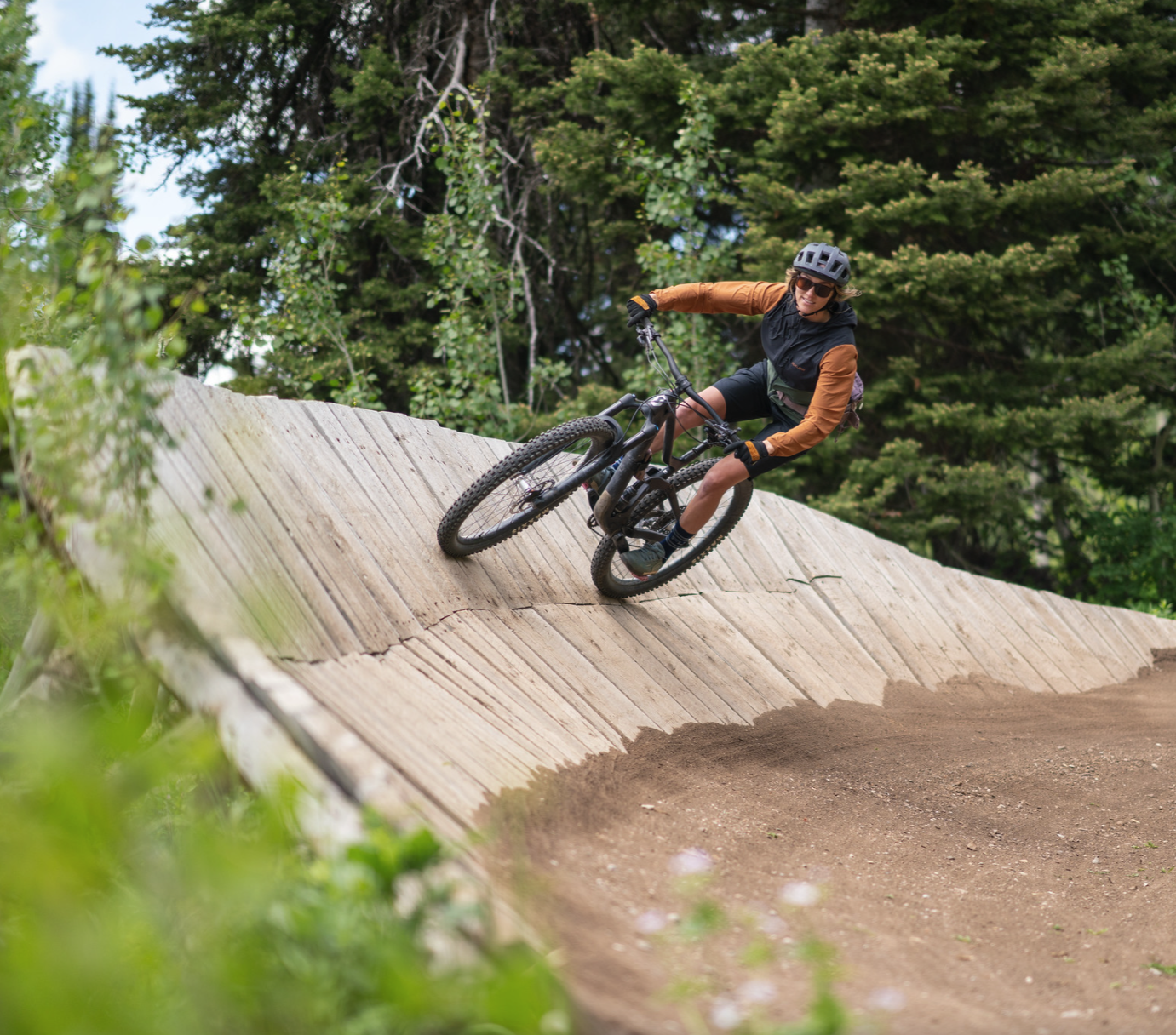 Mountain biker riding a wooden trail curve in a forest setting.