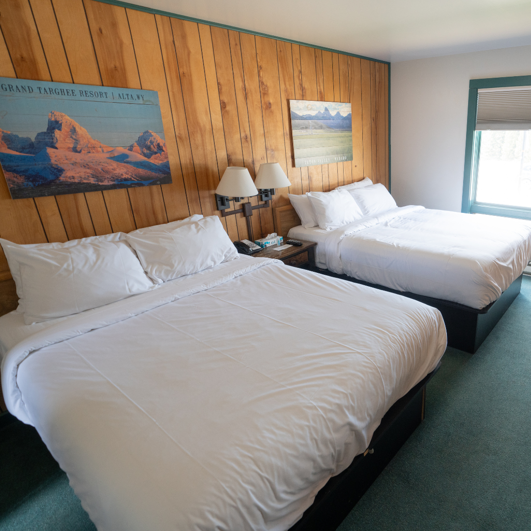 Two neatly made beds in a hotel room with wooden paneling and landscape art.