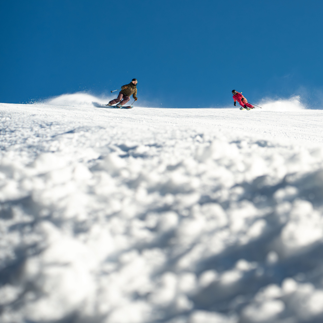 Two skiers on a snowy slope under a clear blue sky.