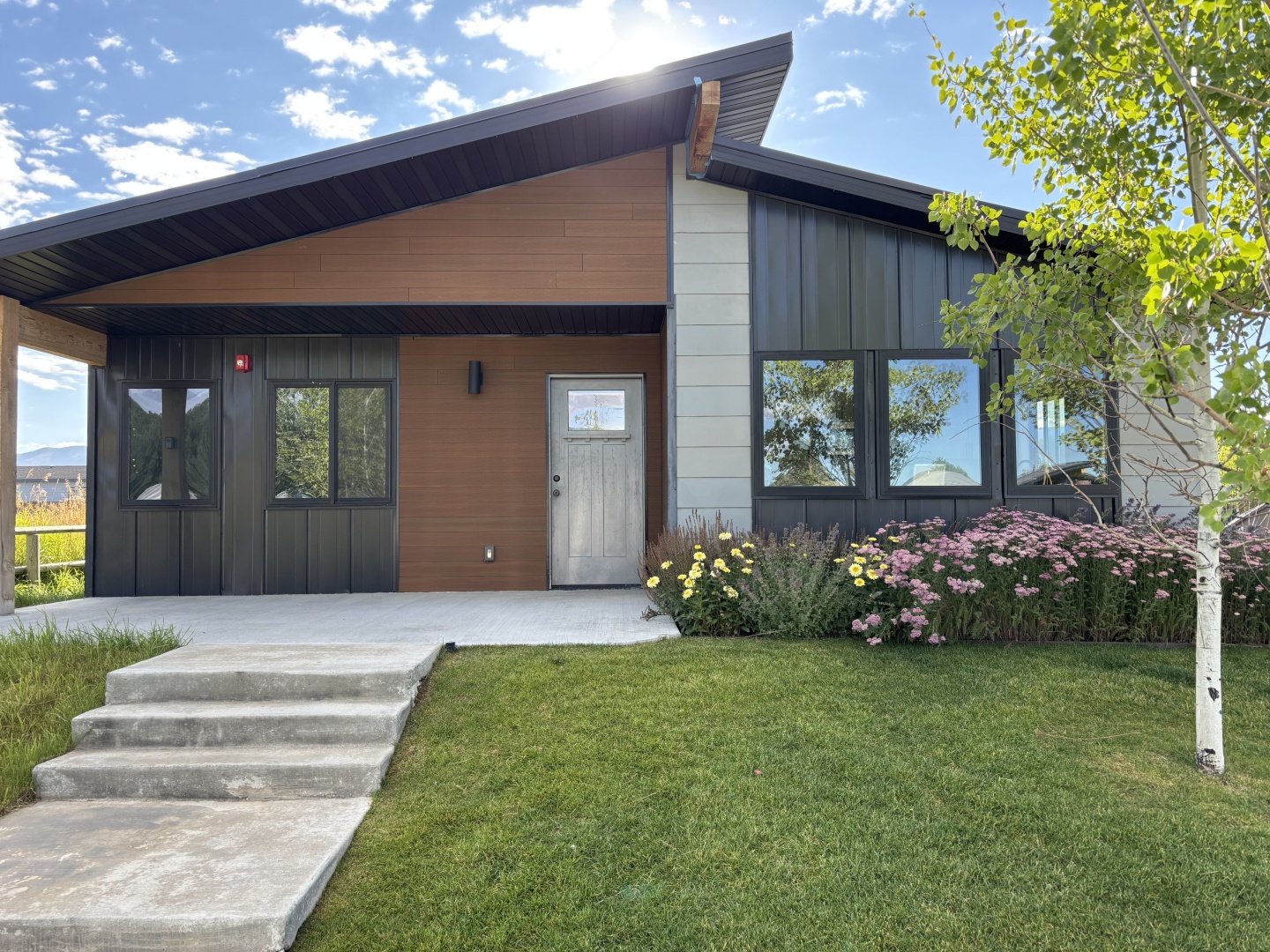 Modern house with sloped roof, front porch, and garden under a blue sky.