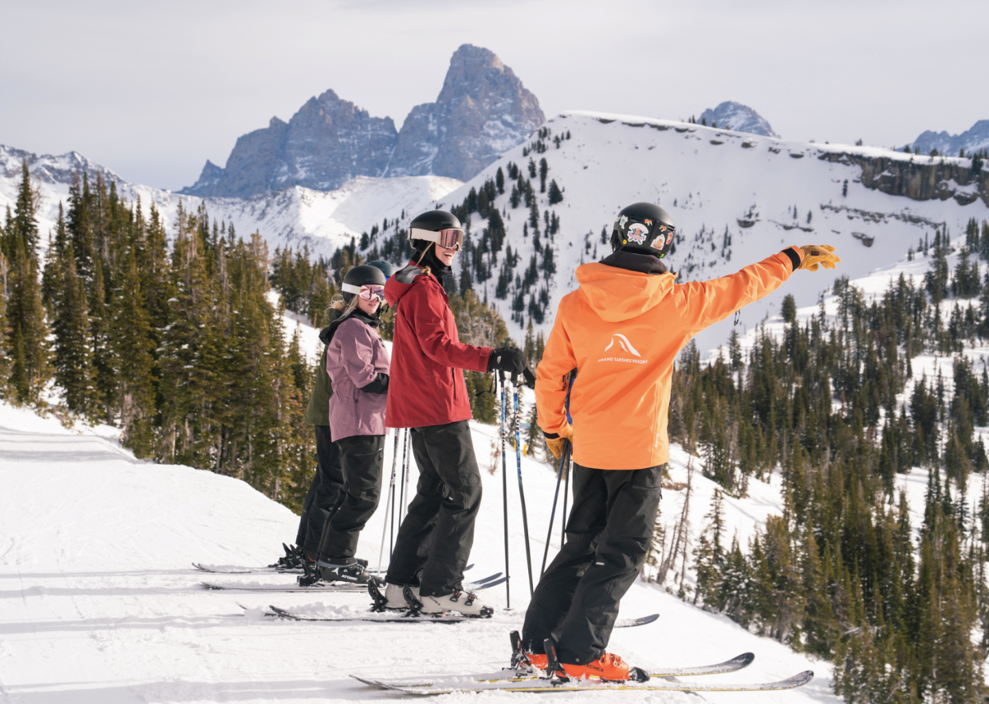 Three skiers on a snowy slope, one pointing to distant mountains.