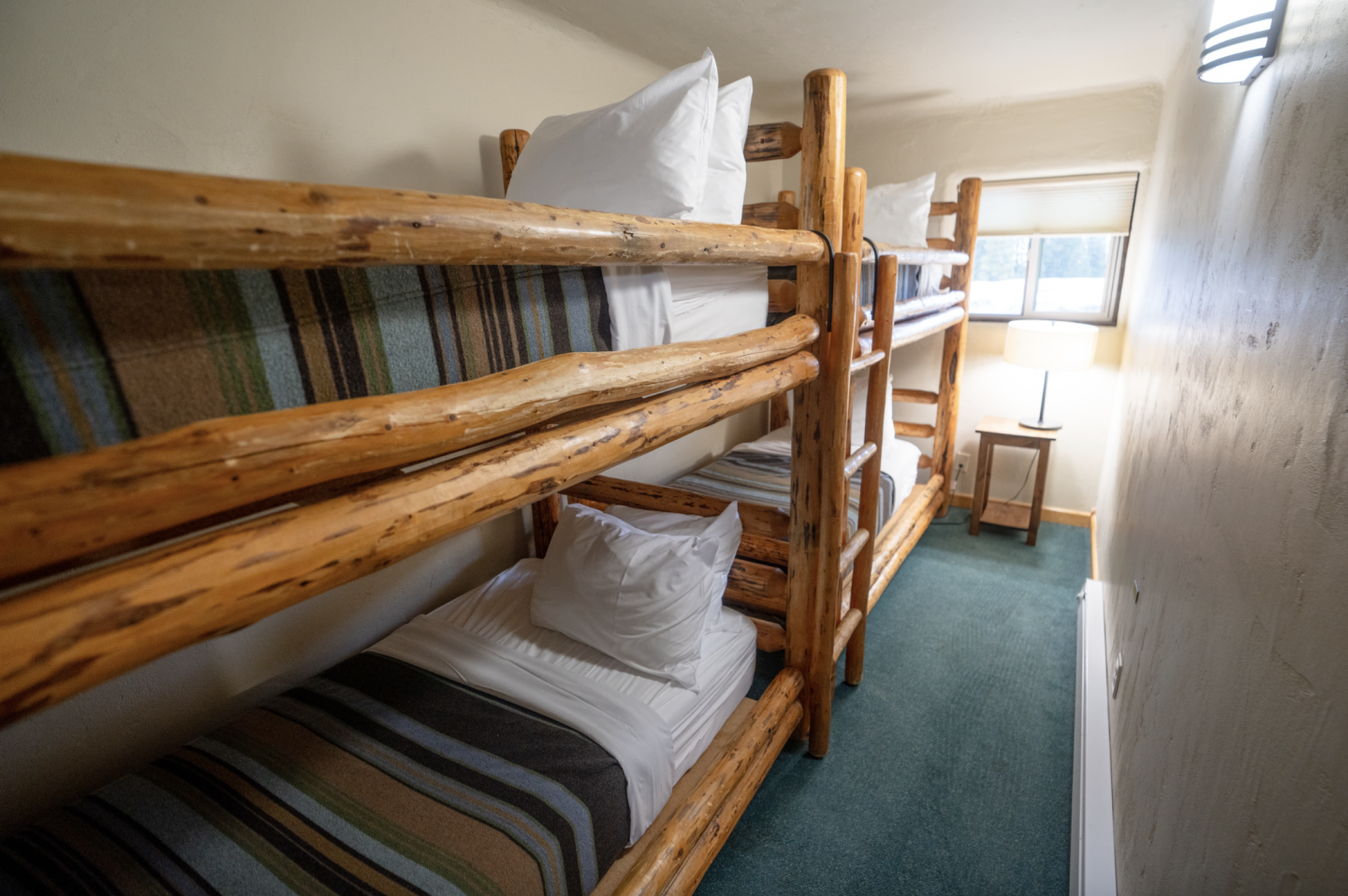 Bunk beds with wooden frames in a narrow, carpeted room with a window.