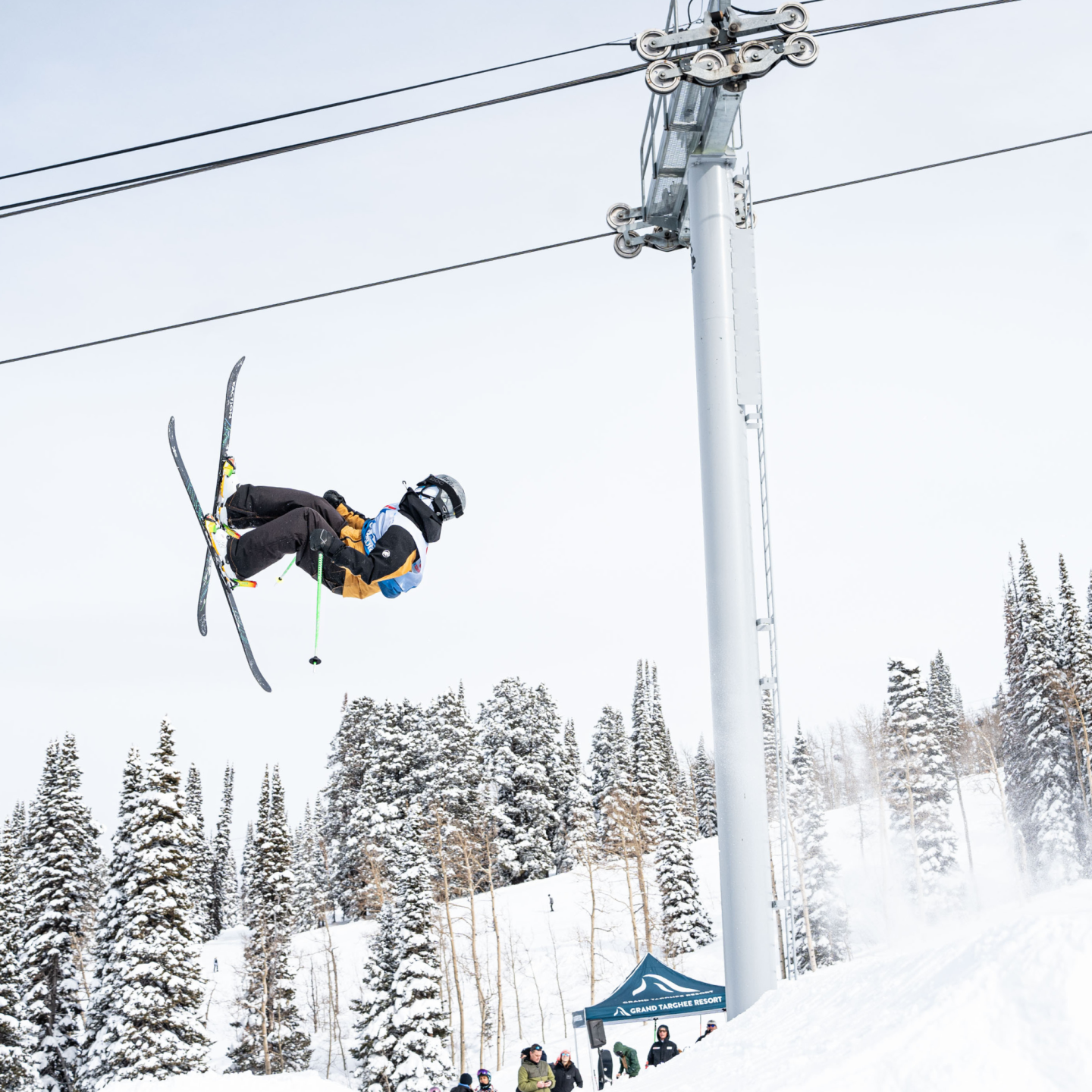 Skier performing a mid-air flip near snowy trees and a chairlift.