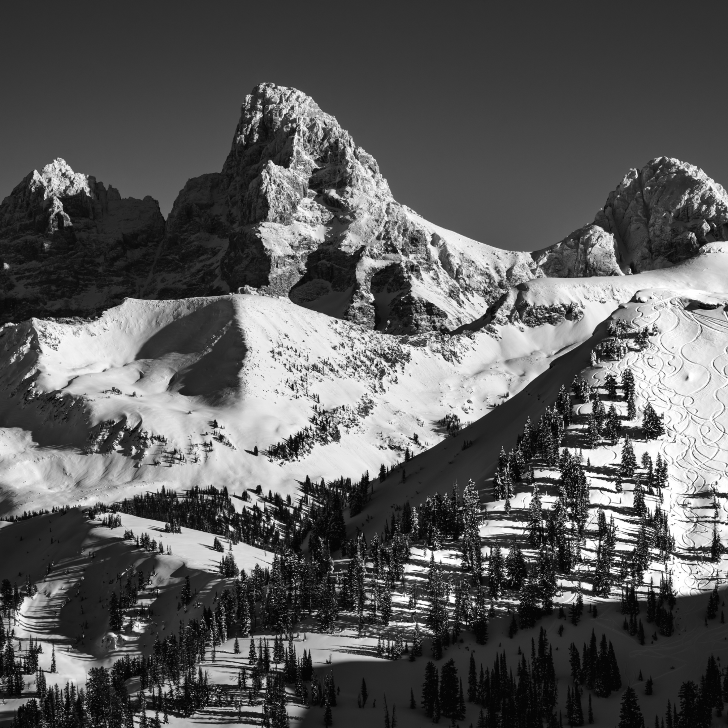 Snow-covered mountain peaks under a clear sky, in black and white.