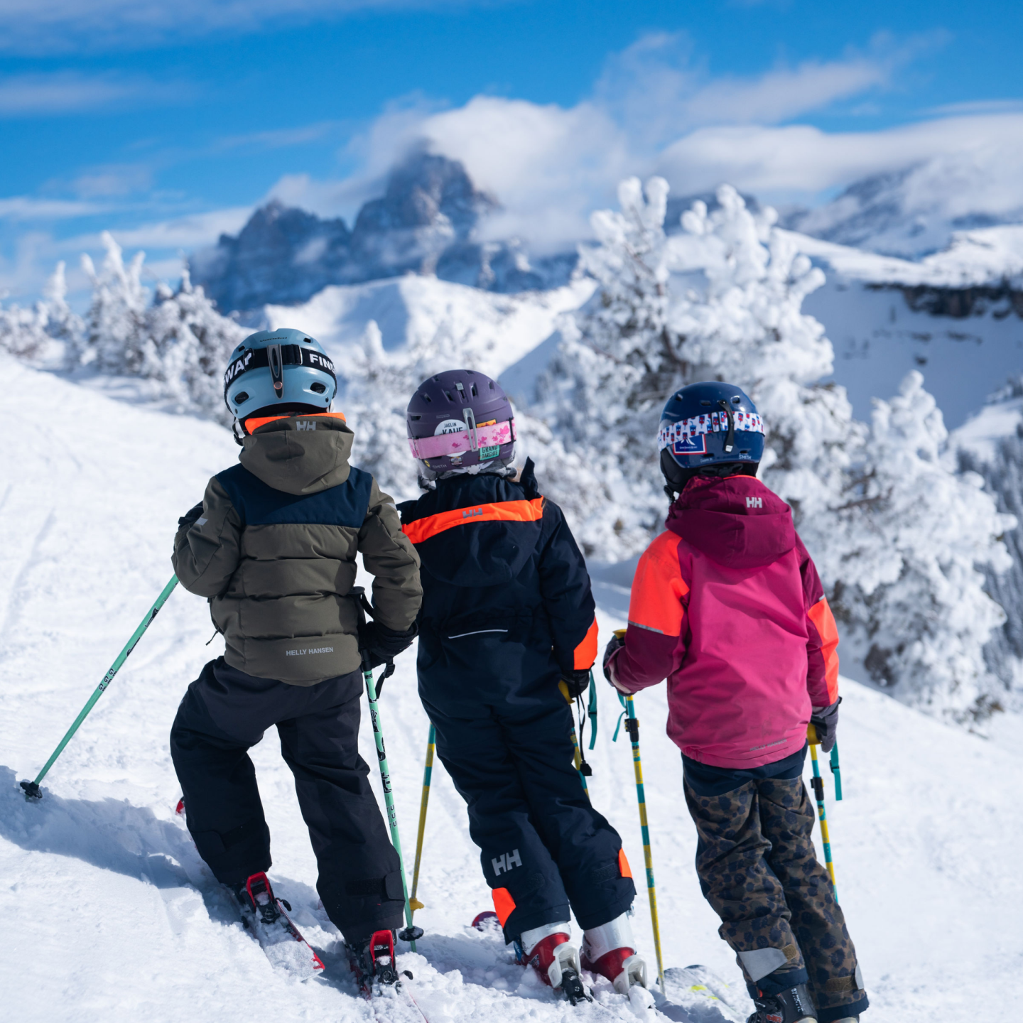 Three children skiing on a snowy mountain with distant peaks.