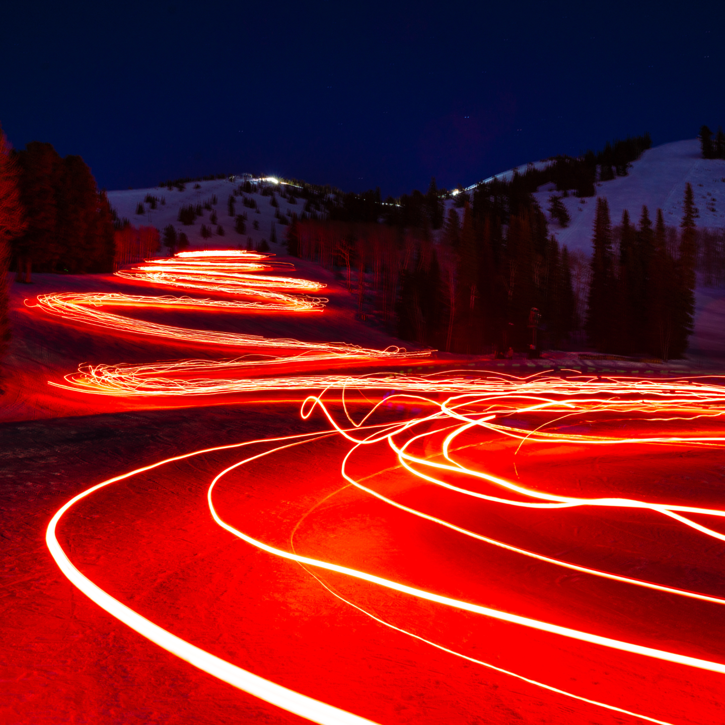 Red light trails on a snowy mountain road at night.